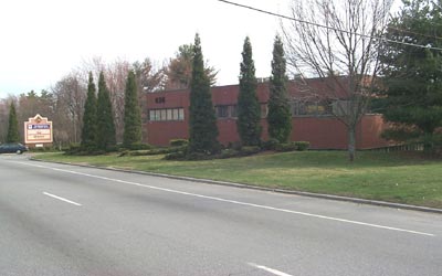 commercial office building with landscaped frontage, evergreen trees, and maintained roadside lawn