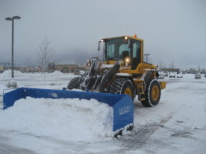 snow removal loader plowing commercial parking lot after winter storm